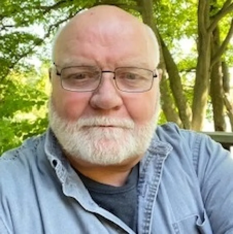Colour photograph of a man, David Monaghan, who wears glasses and has a white beard.