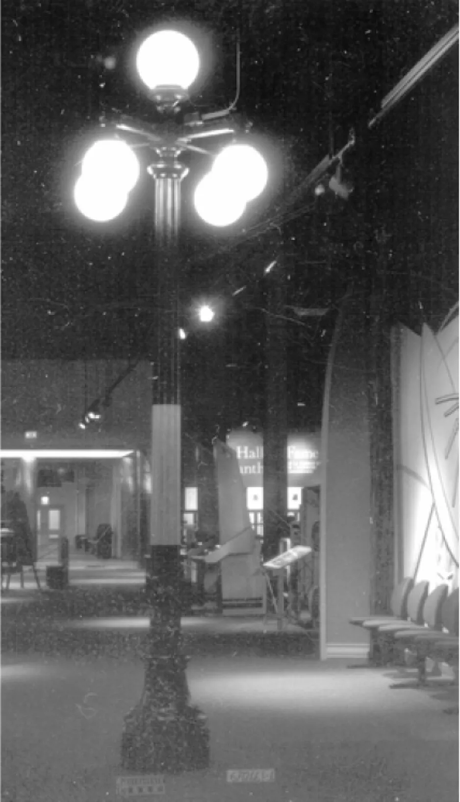 Image en noir et blanc d’un vieux lampadaire surmonté de cinq globes lumineux. Le lampadaire est exposé à l’intérieur d’un musée.  