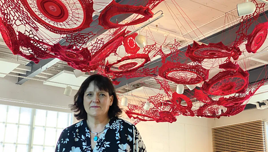 A woman looks directly at the camera as she stands underneath a series of interconnected red crochet circles.