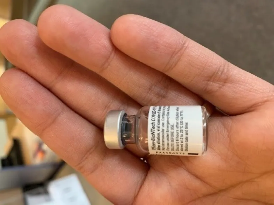 A tiny vaccine vial sits in the palm of a hand.