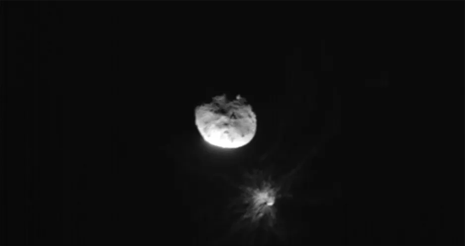 Une image en échelle de gris du centre de l’astéroïde Didymos avec sa lune Dimorphos dans le bas à droite. Dimorphos montre des rayons de poussière et de roche qui s’étendent radialement sur un fond noir. 