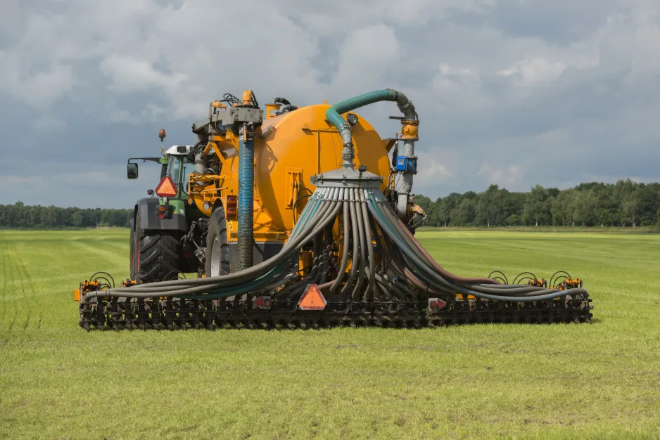 A rear view of a tractor in a field, pulling a large yellow tank on wheels from which multiple pipes emerge and connect to a boom behind the tank.