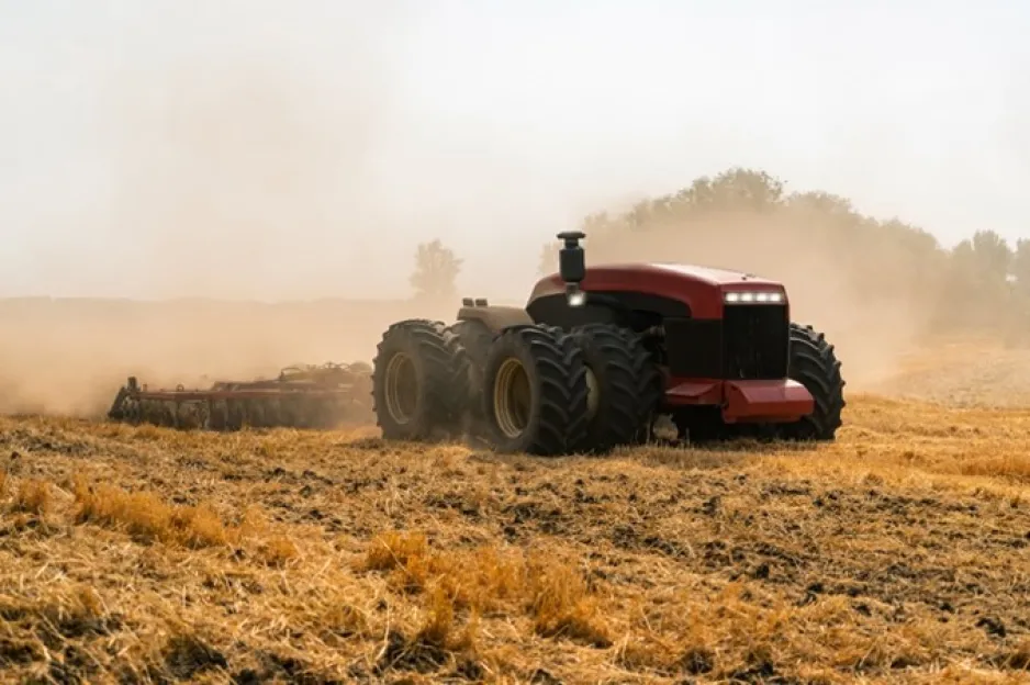 A red tractor with no cab enclosure is pulling soil-working equipment while driving in a field.
