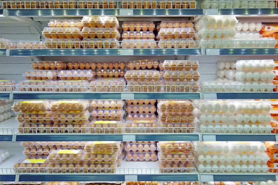Brown and white eggs in clear plastic egg-trays stacked on lit refrigerated shelves in a supermarket