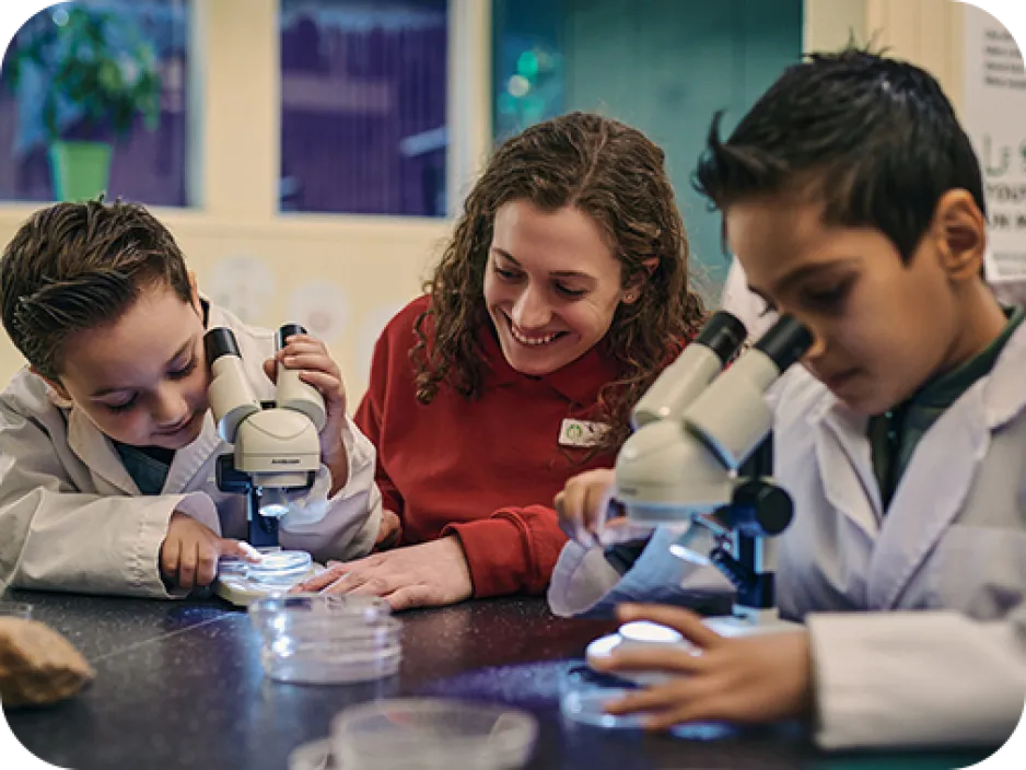 Une guide de musée montre à deux enfants comment utiliser des microscopes.