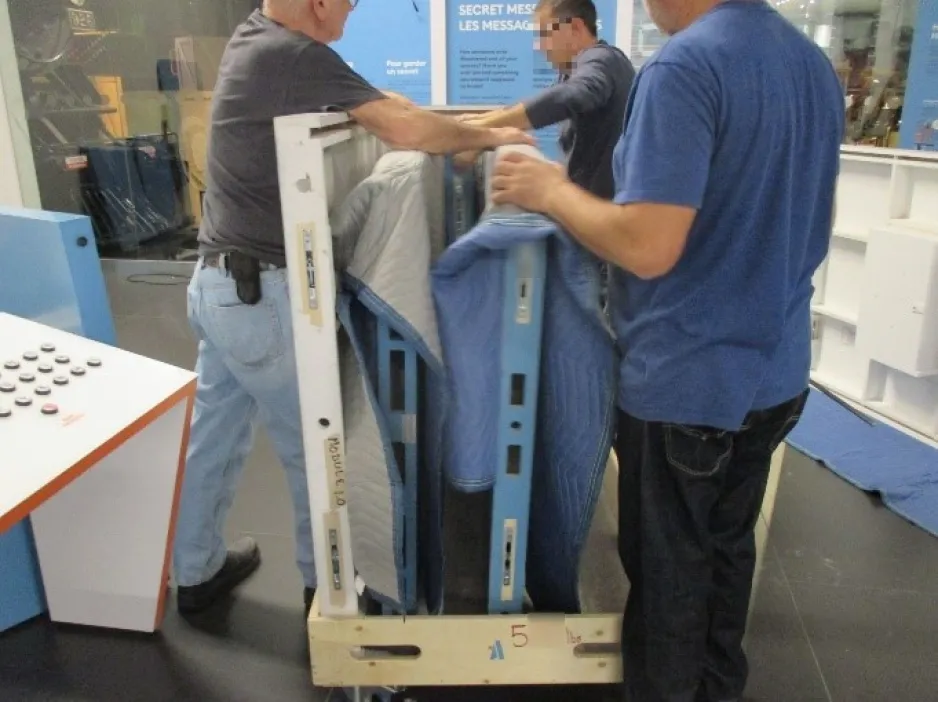 Large, two dimensional wooden pieces of a travelling exhibition are being loaded into a pallet by three men.