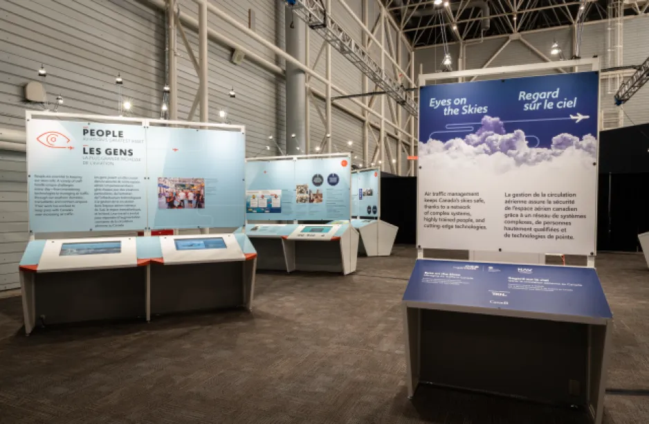 A series of large exhibition panels are set up inside a museum space. The title “Eyes on the Skies” is visible on the nearest panel.