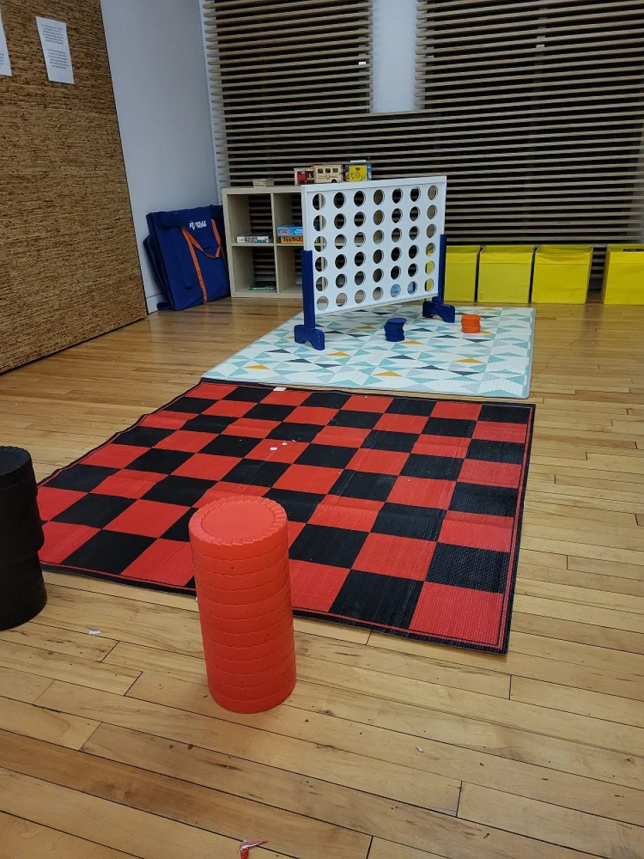 Un jeu de dames surdimensionné et un jeu Connect 4 sont installés sur un sol en bois dur.