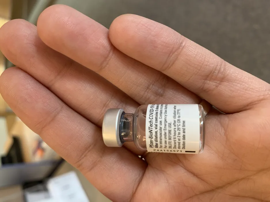 A close- up of a small glass vial containing the Pfizer-BioTNTech COVID-19 vaccine, sitting in the palm of a hand.