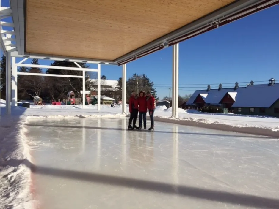 Three people stand in the middle of an outdoor skating rink.