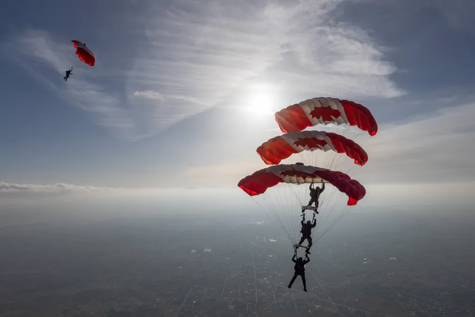 Quatre personnes flottant sur des parachutes rouges et blancs du drapeau canadien dans un vaste ciel bleu.