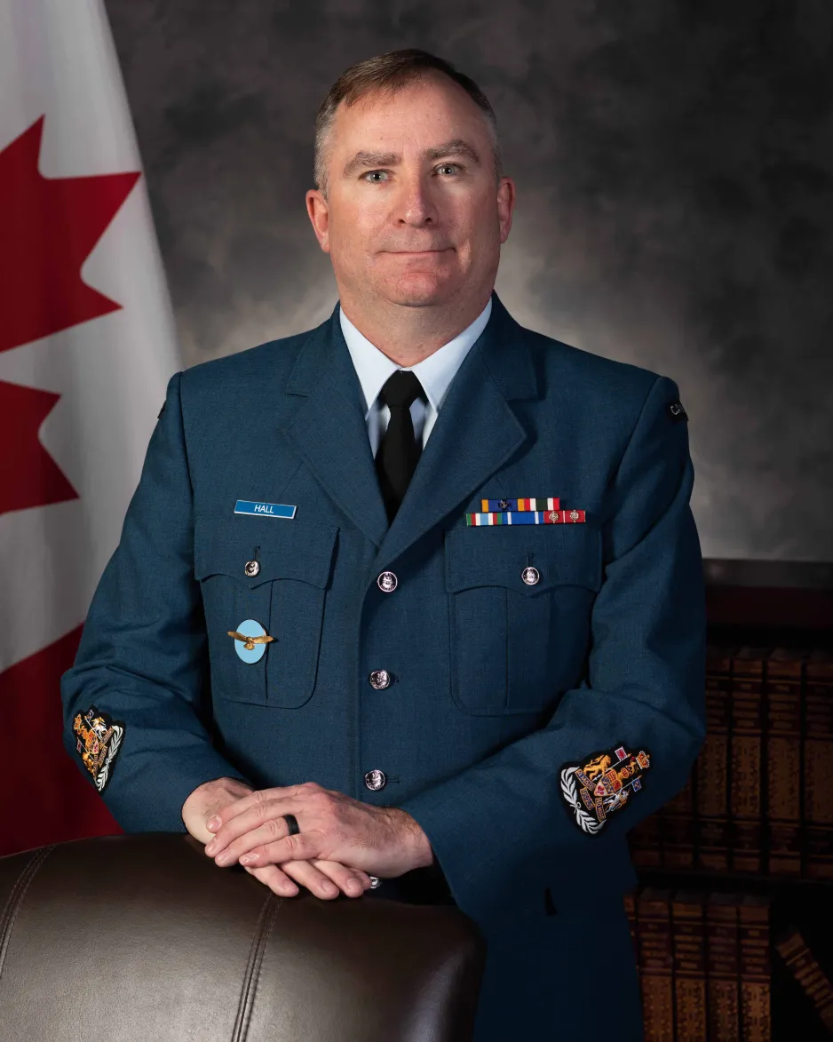 Une personne souriante en uniforme de l'ARC est assise devant le drapeau canadien.