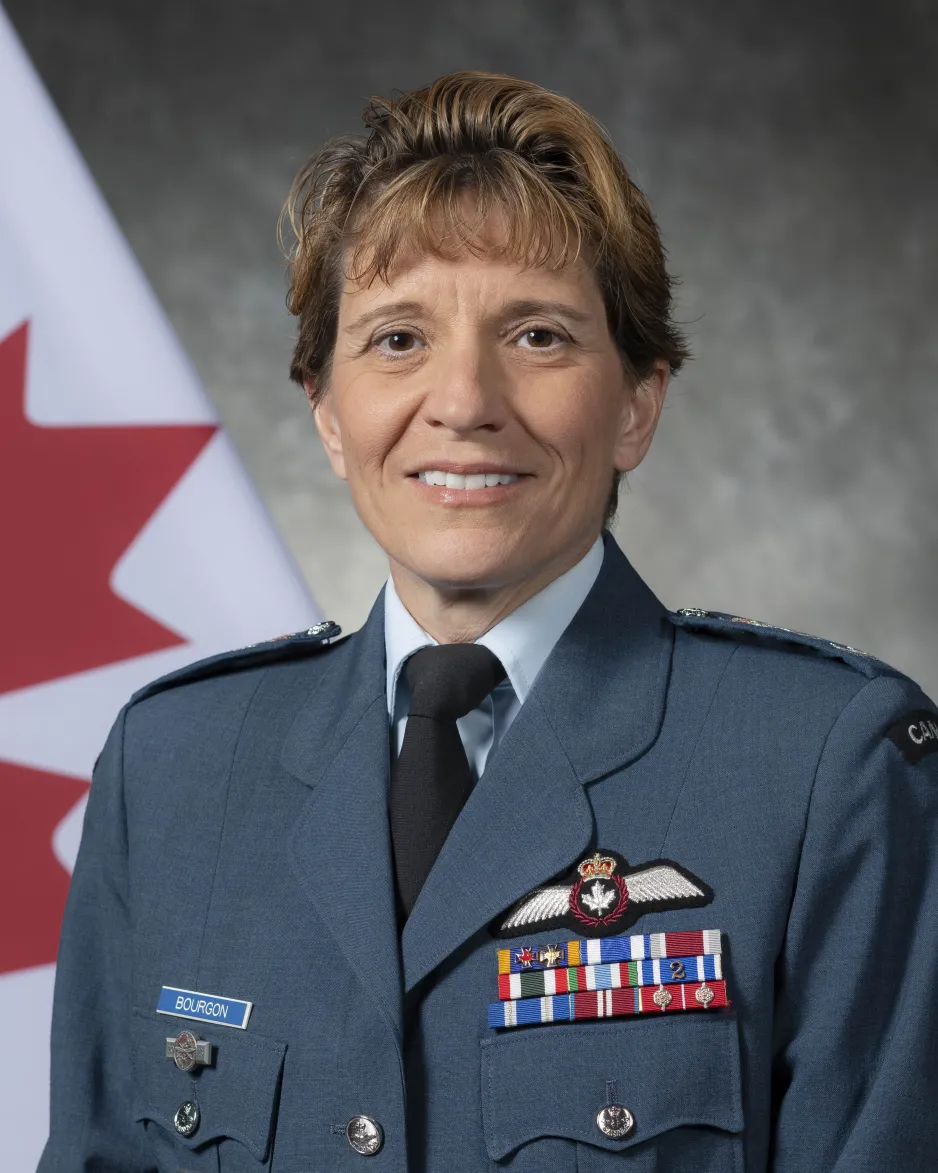 Une personne souriante porte un uniforme bleu de l'ARC et se tient devant le drapeau canadien.