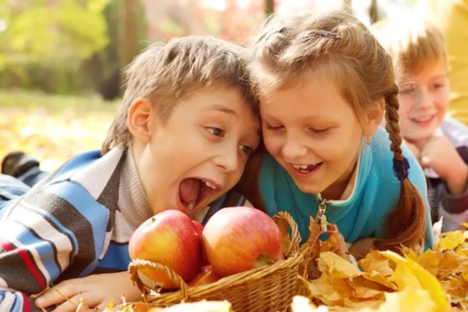 Vue rapprochée d'un garçon et d'une fillette penchés au-dessus d'un panier de pommes. Le garçon fait semblant de croquer dans une pomme tandis que la fille rit.