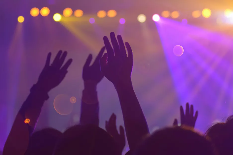 Silhouettes of hands in the air at a dance club. In the background are stage lights and purple lasers.