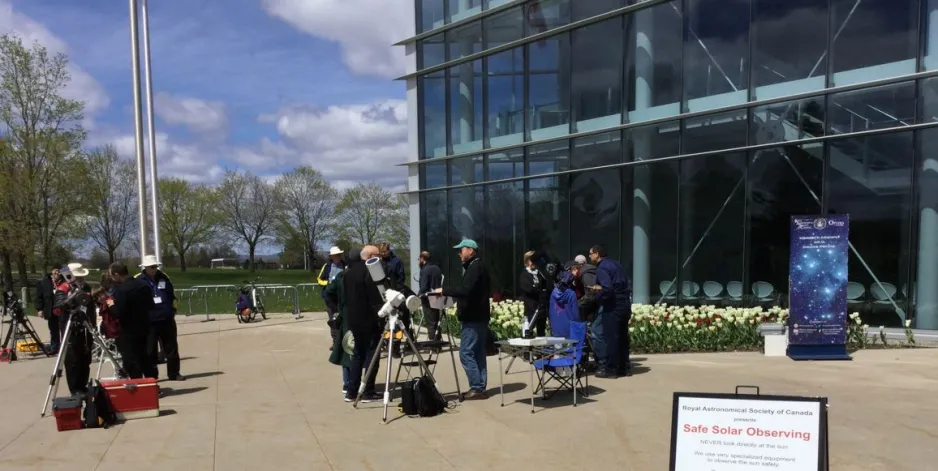 Un groupe de personnes se tient devant le Musée de l'aviation et de l'espace du Canada avec des télescopes solaires.