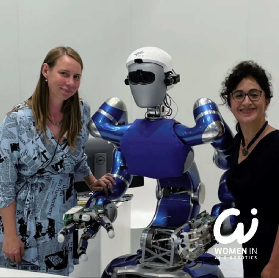 Deux femmes se tiennent de chaque côté d'un robot humanoïde bleu et argenté.