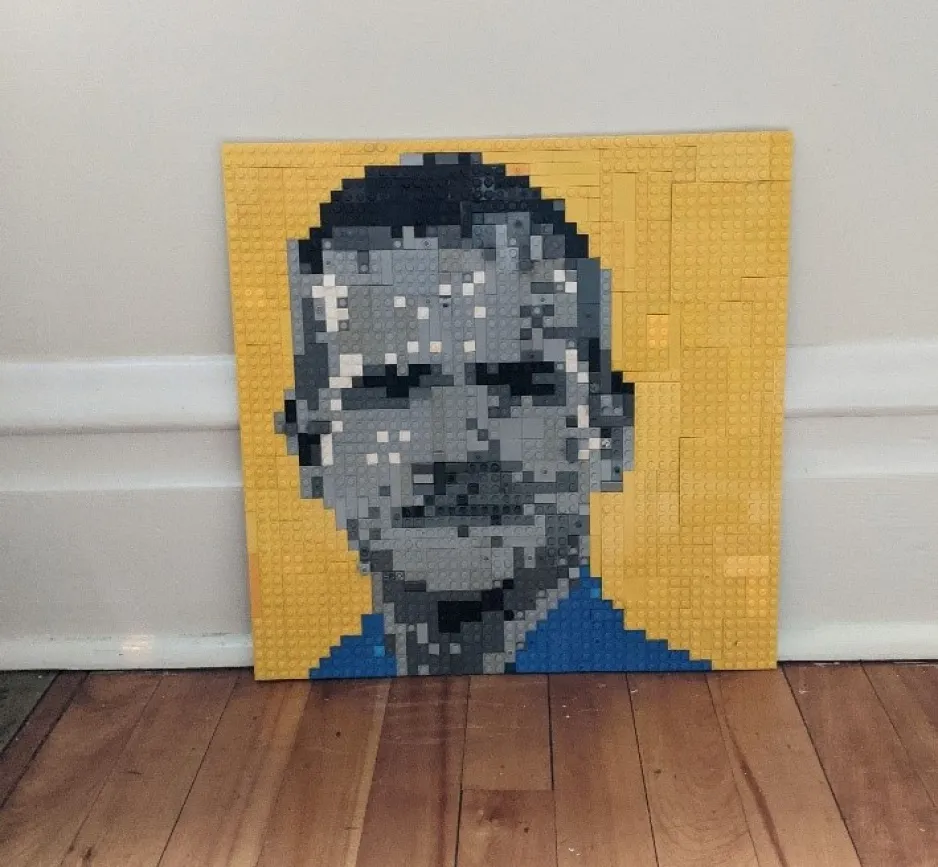 A portrait-style LEGO creation features the face of Canadian astronaut Chris Hadfield. The creation has a yellow background, and the face is made of grey, black, and white LEGO blocks.