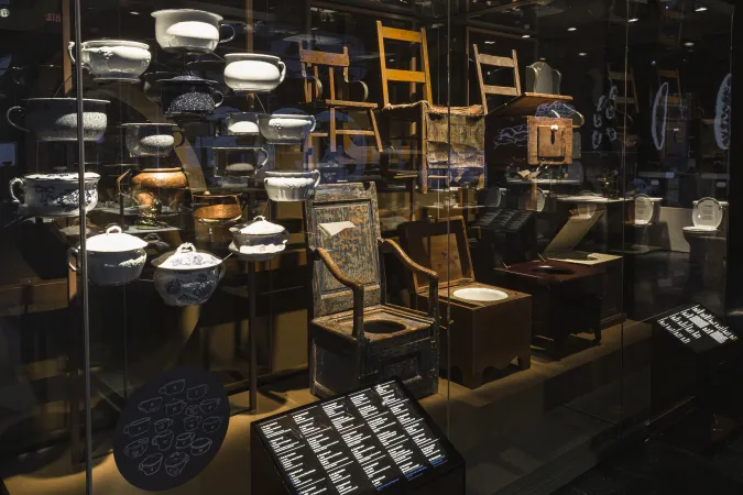 A display case with a variety of chamber pots and commode seats.