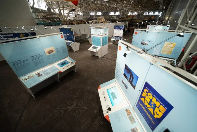 An aerial view of the exhibition, showing many modules; a module displays a panel containing a “Come From Away” poster in the foreground.