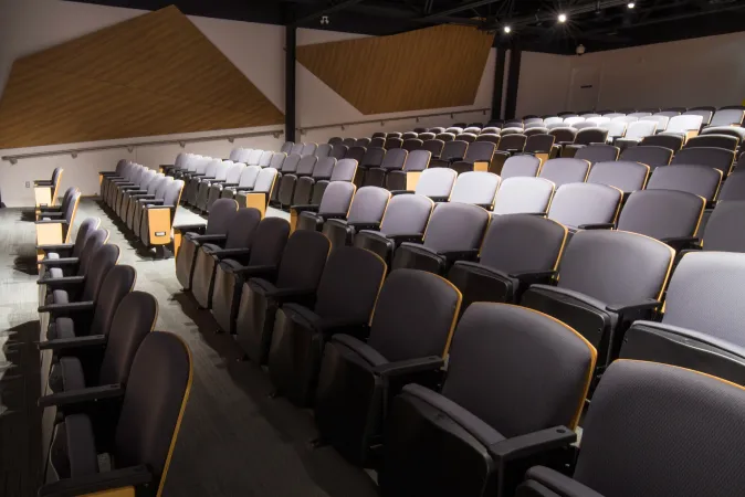L’auditorium du Musée des sciences et de la technologie du Canada, vu du côté de la salle. Des rangées de sièges rappelant ceux d’une salle de théâtre, en tissu violet, s’alignent de chaque côté d’un escalier. Il y a quelques places à l’avant, au bas des escaliers, sans fauteuils pour accommoder les personnes à mobilité réduite. 