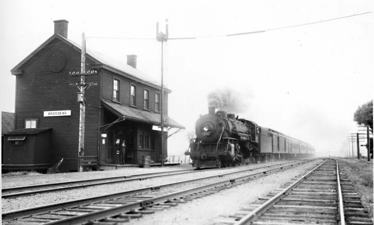 Black and white photograph showing a steam locomotive approaching a station.