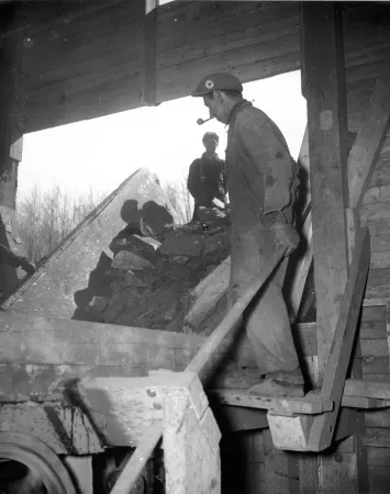Des travailleurs déversent du minerai de fer sur le concasseur pour un projet minier d’urgence en temps de guerre dans l’est du Canada.