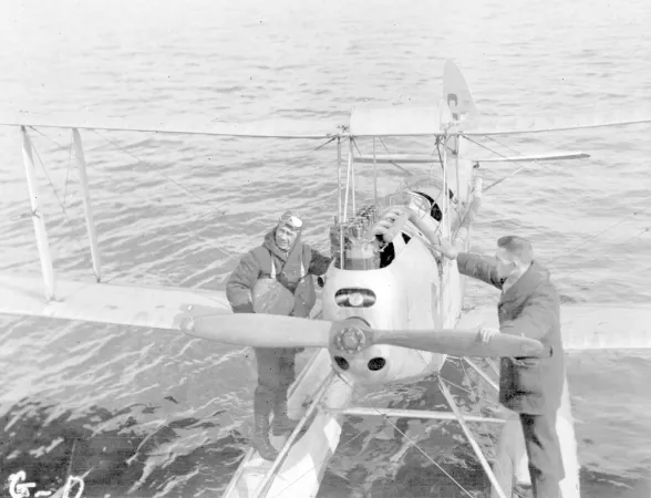 Black and white photograph of two Expedition members standing on pontoons of Moth plane. 