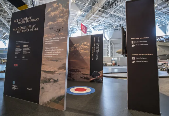 Exhibition panels create an enclosed area, with a large bull-eye sticker is on the floor.  The foreground panels are dark blue with white text.  
