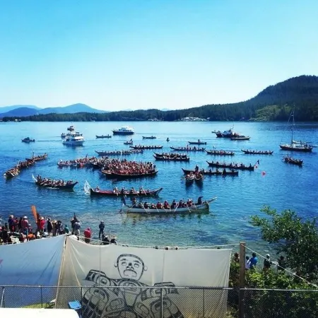 Canoes hover around a beach shore in Bella Bella, British Columbia during the Qatuwas in 2014