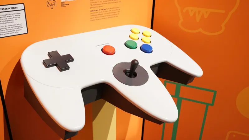 Une manette de jeu Nintendo blanche surdimensionnée est fixée sur un panneau d’exposition orange.