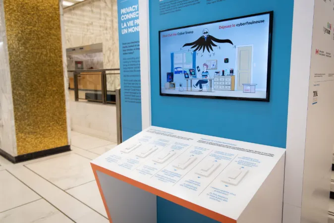 A large screen with a cyber-thief pictogram is mounted on an exhibition module.  Below the screen is a table with a number of switch and blue instructional text.