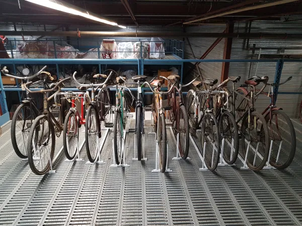 A series of bicycles stand in a line on a metal rack.