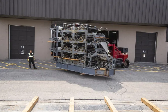 Un lève-palette de 35 tonnes métriques soulève la presse d’imprimerie Goss et la place sur un camion à plate-forme.