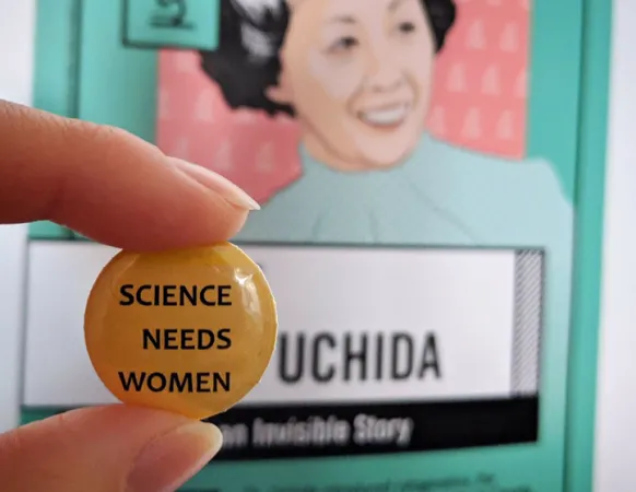 A pin with the words ‘Science Needs Women’ being held up in front of a Women in STEM Poster of Irene Ayako Uchida.