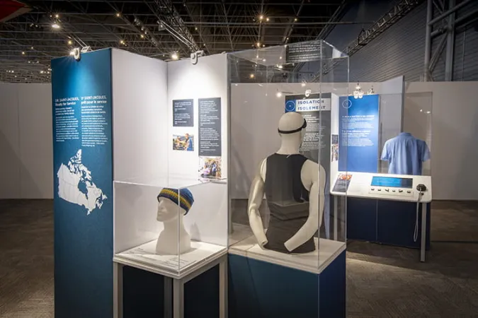 An exhibition module containing two artefacts is in the foreground. A knitted toque and a black shirt paired with a black headband are contained within display cases.
