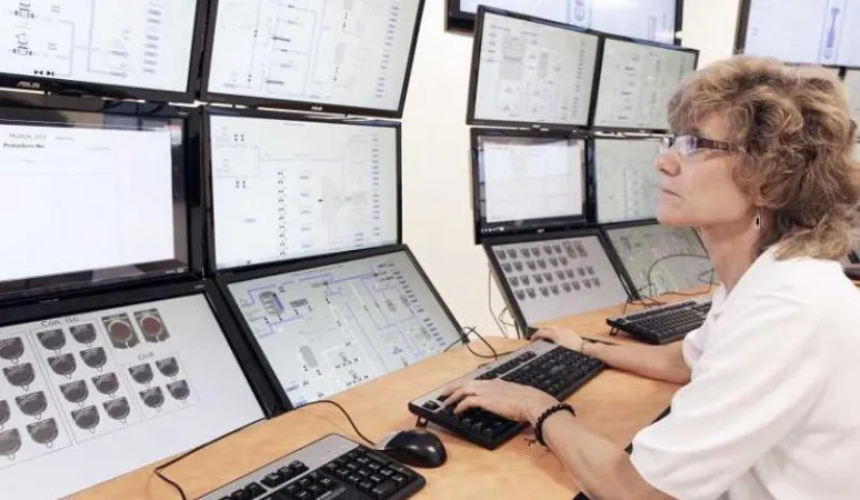 Salle de commande du PRM NuScale : une opératrice de salle de commande examine des données à l’écran, dans une centrale à 12 réacteurs.