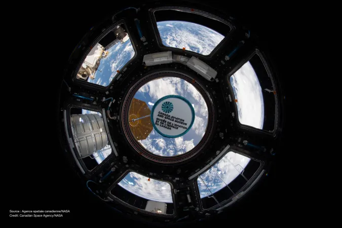Petit écusson portant l’inscription « Musée de l’aviation et de l’espace du Canada », photographié devant la coupole de la Station spatiale internationale, avec la Terre à l’arrière-plan.