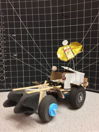 A rover prototype, made of various materials, sits on a desk.