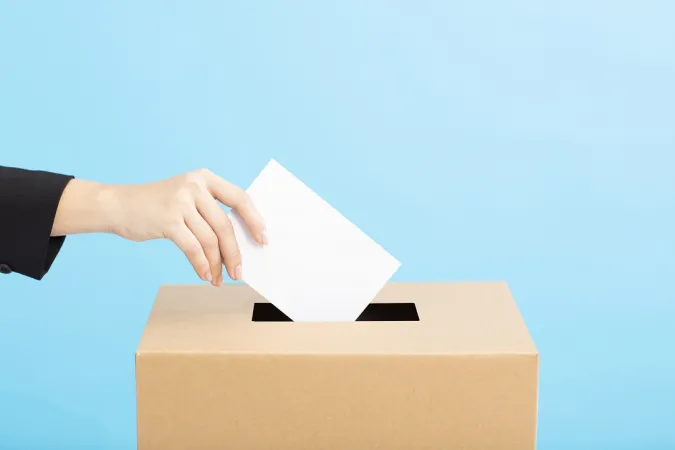Main de femme tendant un bulletin de vote au-dessus d’une urne