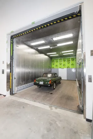 A green sports car looks tiny as it sits inside the oversized freight elevator.