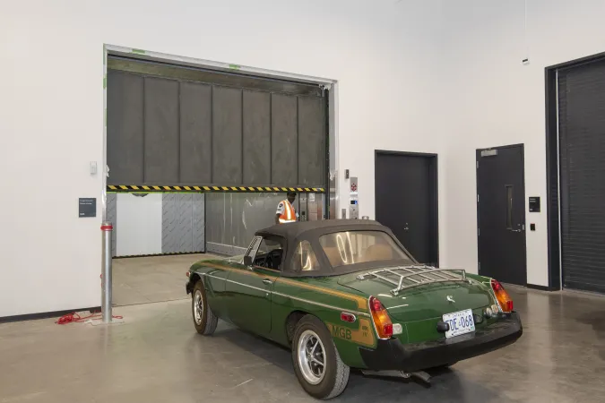 A worker opens the large elevator door, as a green sports car sits in front.