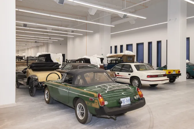 A rear view of a green sports car, lined up with dozens of other vehicles in a large storage space.