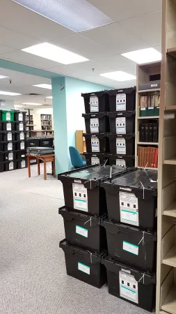 Photo shows several stacks of black bins in the old Library used for books as part of the packing