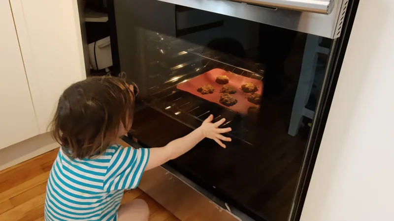 A young child watches cookies bake in an oven.