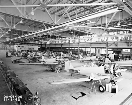 Photo en noir et blanc de l’assemblage d’aéronefs dans l’usine de Noorduyn. Il manque encore des pièces, notamment des ailes, aux avions alignés sur le sol.