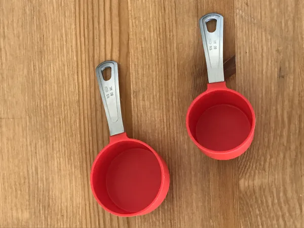 Two small red plastic measuring cups sit on top of a wooden table. 