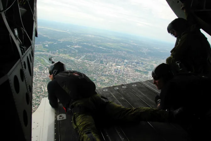 Deux hommes en tenue militaire se préparent à sauter en parachute d’un avion.