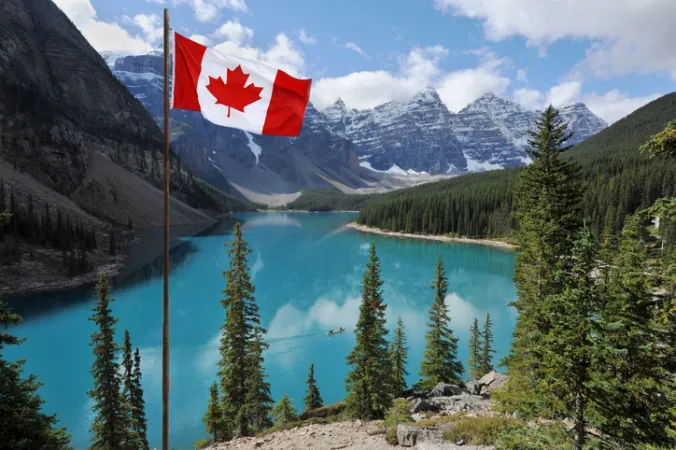 The Canadian flag, set against the backdrop of a clear, blue lake and mountains in Banff National Park, Alberta.
