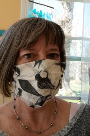 A close-up of a woman wearing a mask she made out of white fabric, with a crow pattern on it.